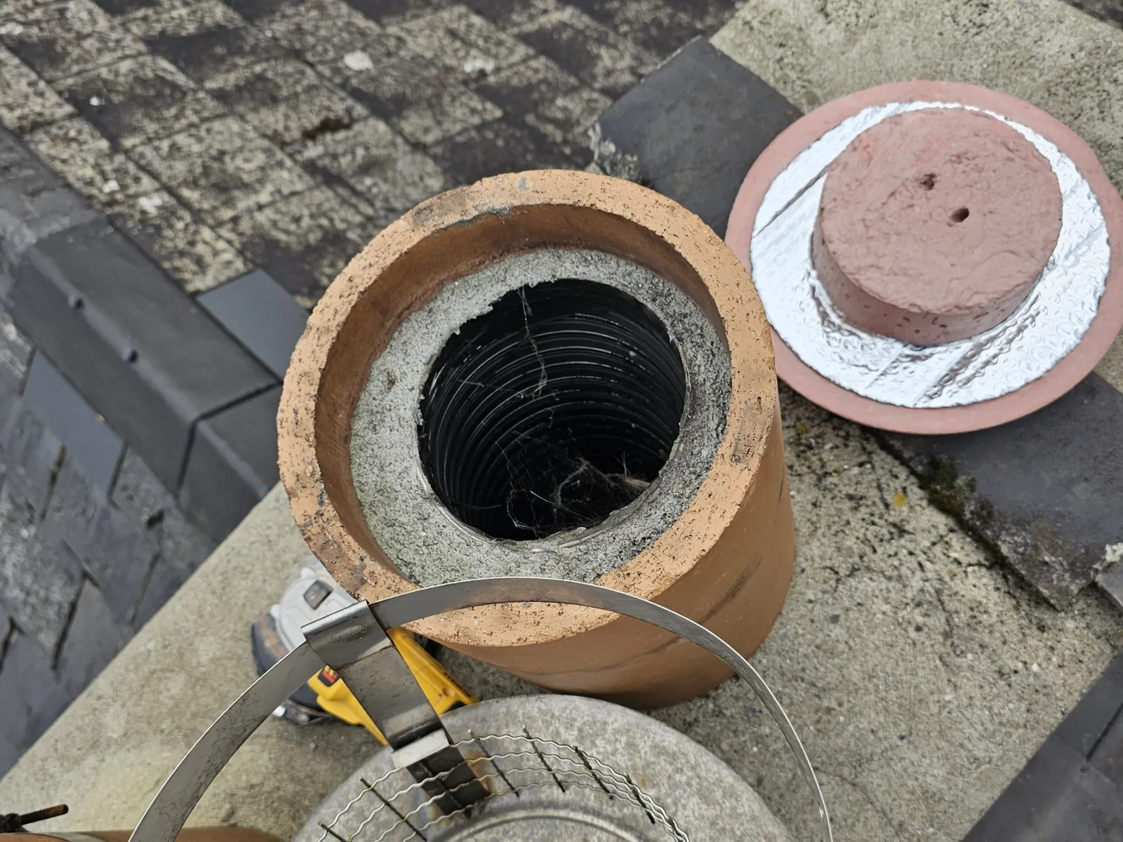 Chimney pot with a flexible flue liner, cowl removed and the new cap ready to fit