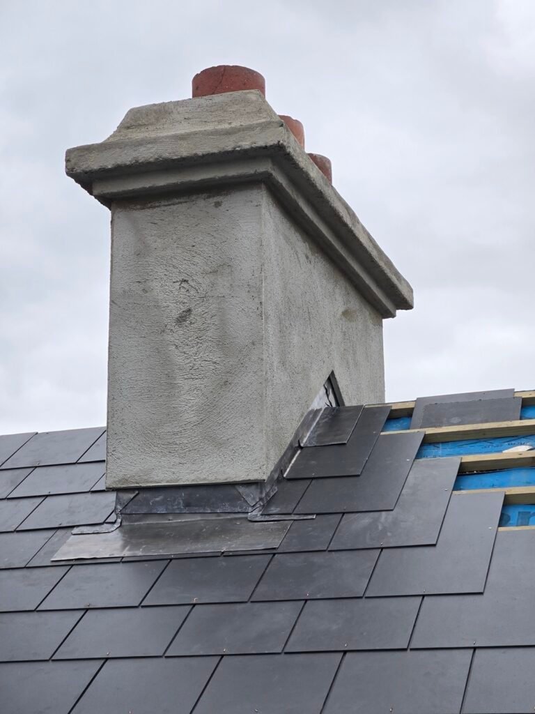 Lead apron and stepped flashing to a rendered chimney on a slate roof