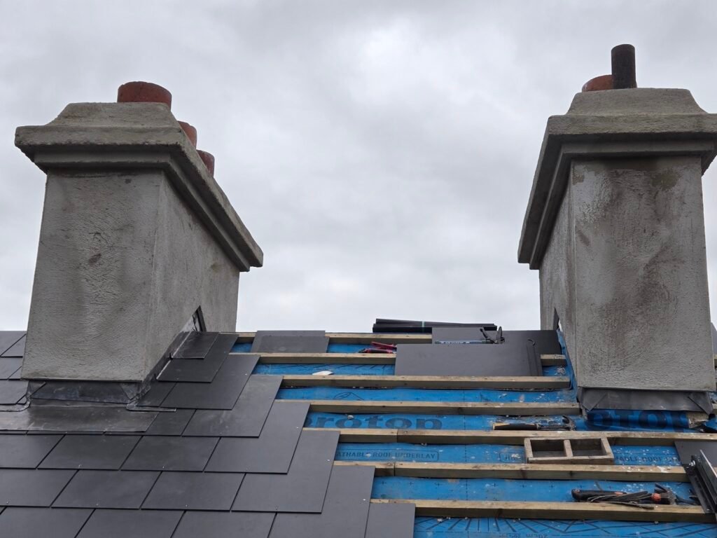 Lead chimney flashings being installed on two stacks during a slate re-roof
