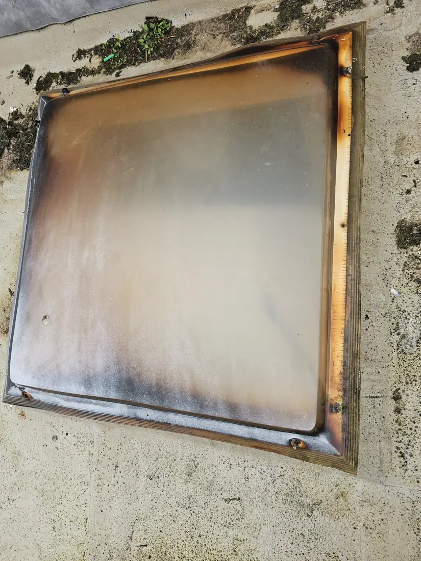 Old yellowed flat roof skylight dome with scorch marks along the edge, removed before replacement
