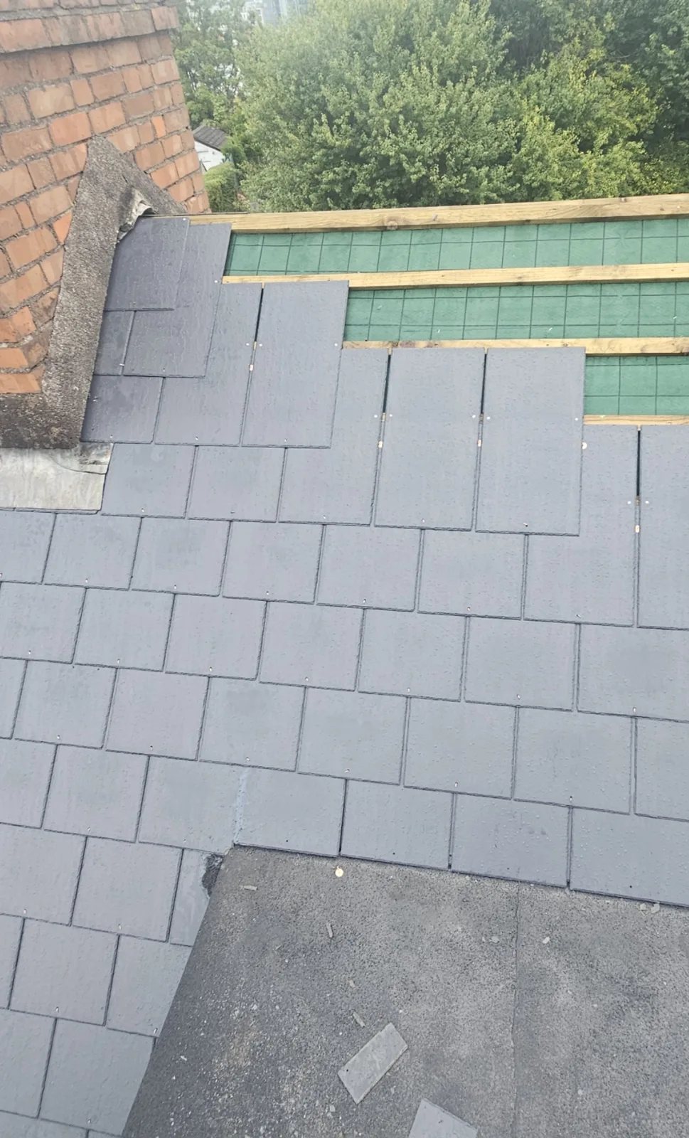 New fibre cement slates being fixed next to a brick chimney, battens and membrane above