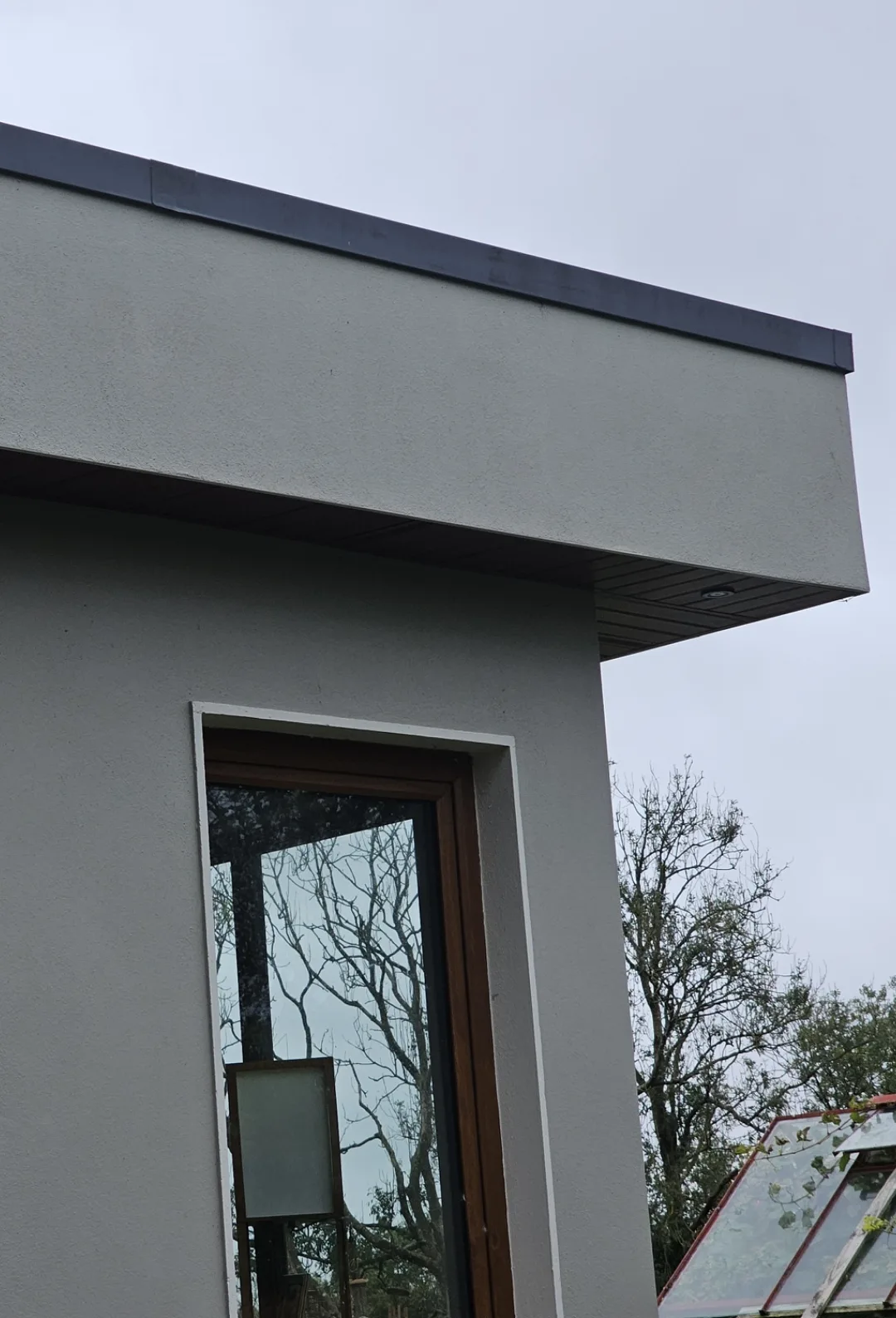 Finished flat roof with dark edge trim and soffit on a rendered extension