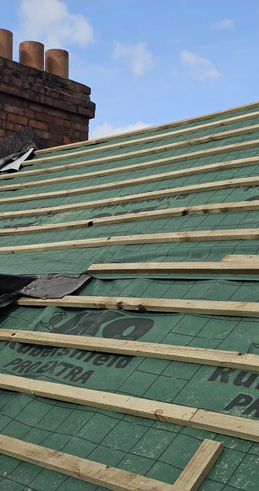 New treated battens fixed over breathable roofing membrane next to a brick chimney