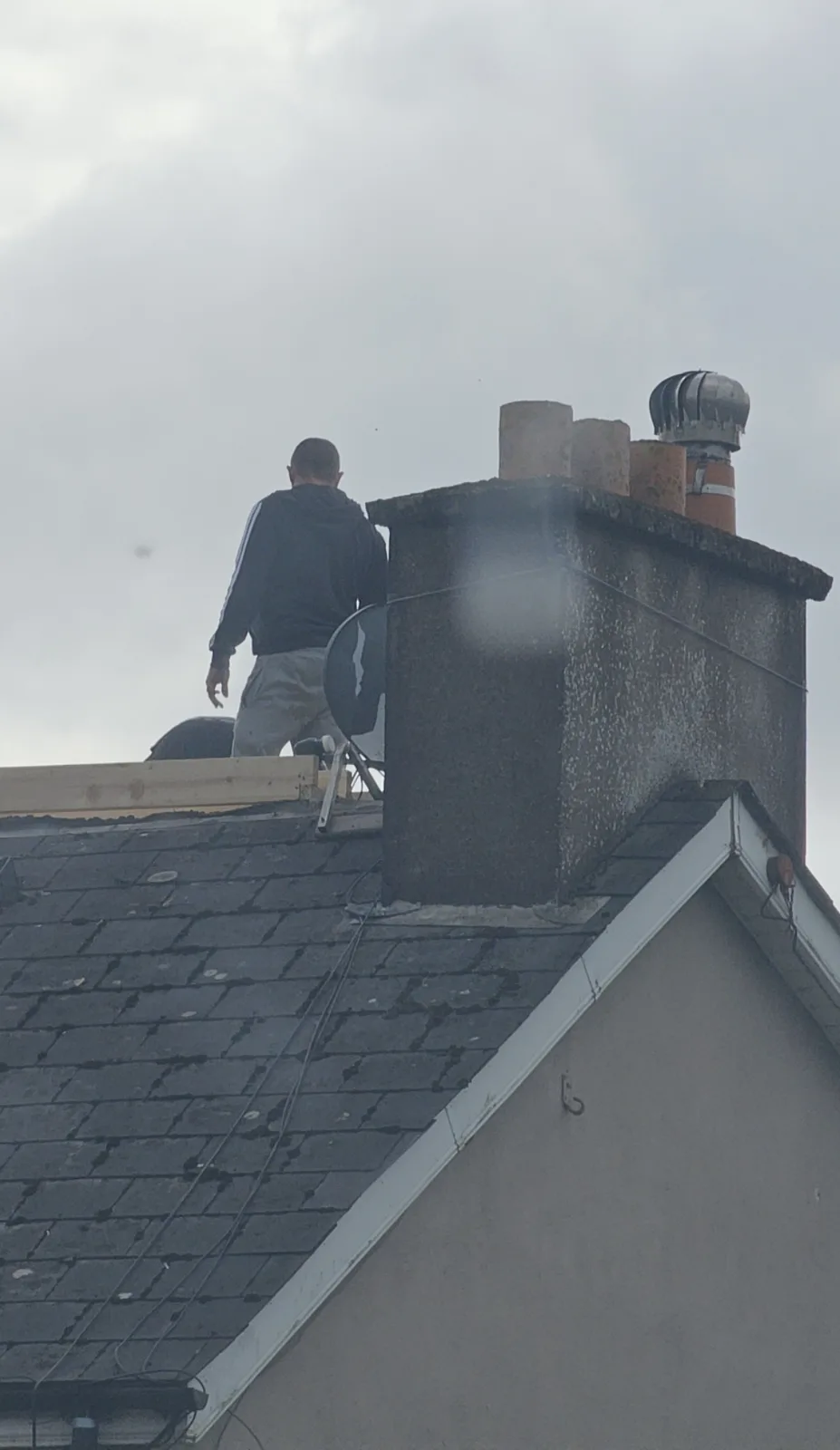 Roofer working beside a rendered chimney on an old slate roof before re-roofing