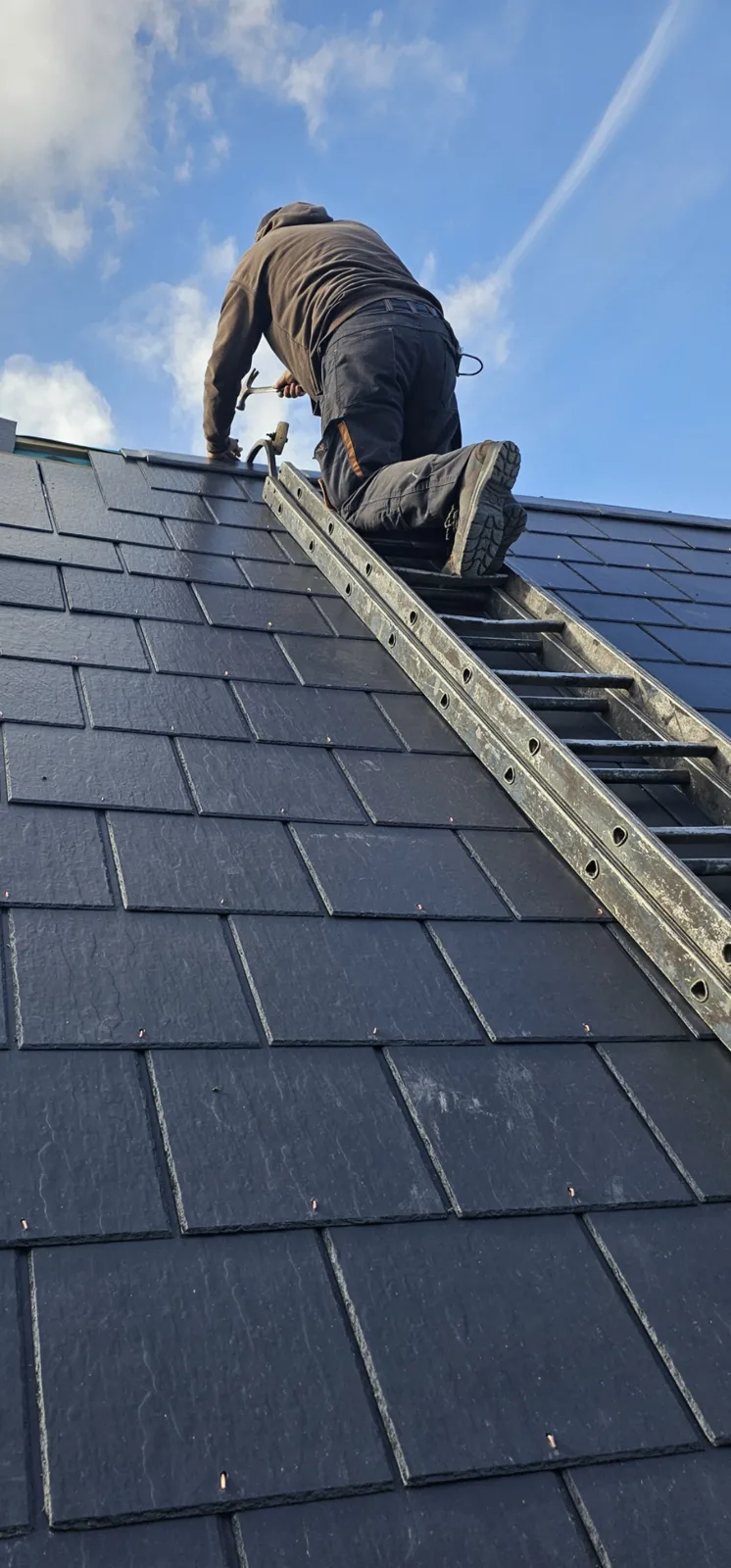 AltRoofing roofer on a roof ladder fixing new slates near the ridge