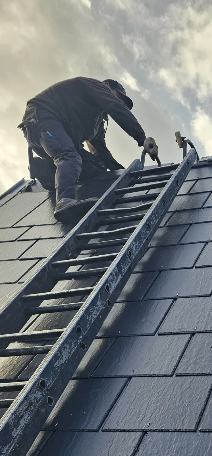 Roofer on a roof ladder working at the ridge of a newly slated roof