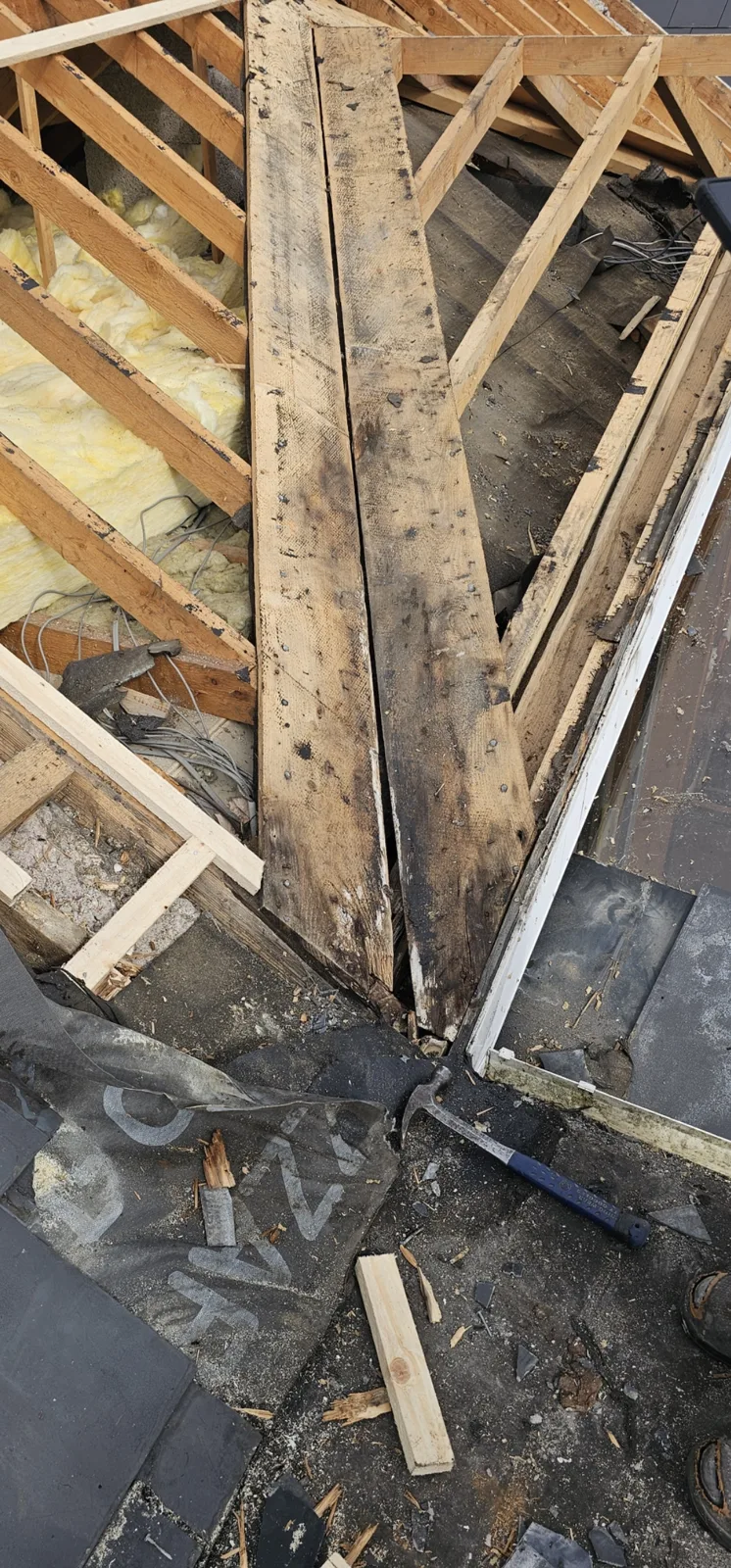 Rotten roof valley boards exposed after stripping, with rafters and attic insulation visible